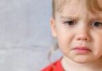 kid crying. the face of a cute little upset four year old baby boy in tears. children's grief. gray concrete wall background. space for text