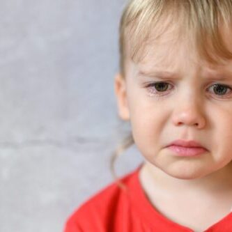 kid crying. the face of a cute little upset four year old baby boy in tears. children's grief. gray concrete wall background. space for text