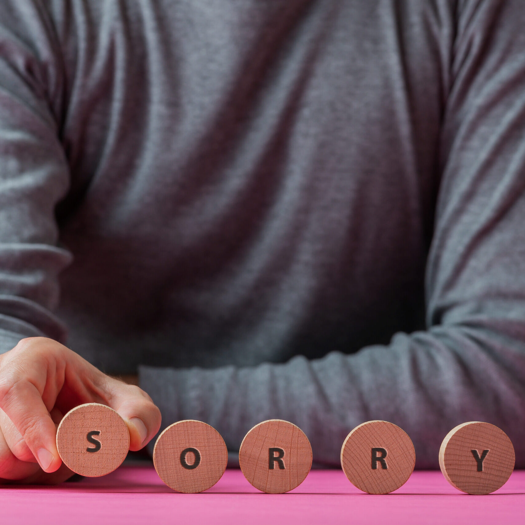 Front view of a man making a Sorry sign spelled on wooden cut circles.